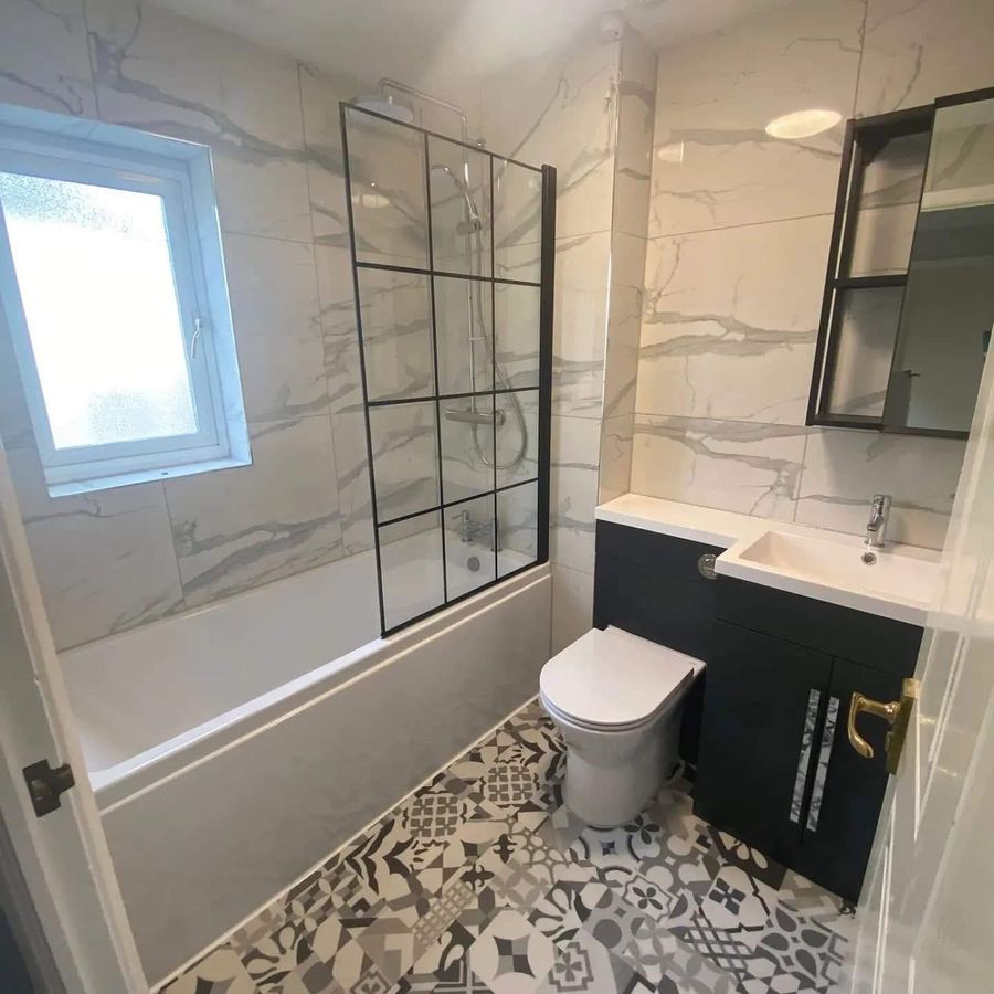 A bathroom by Jaden: bath with a black-grid screen, marble-effect walls, a dark vanity unit and a patterned floor