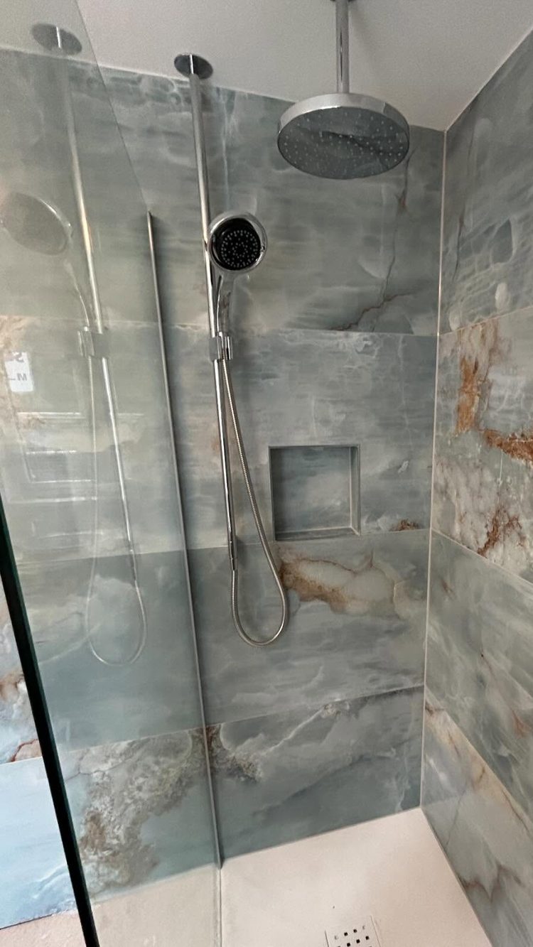 A walk-in shower Jaden tiled in onyx-effect stone, with a recessed niche and a ceiling rainfall head