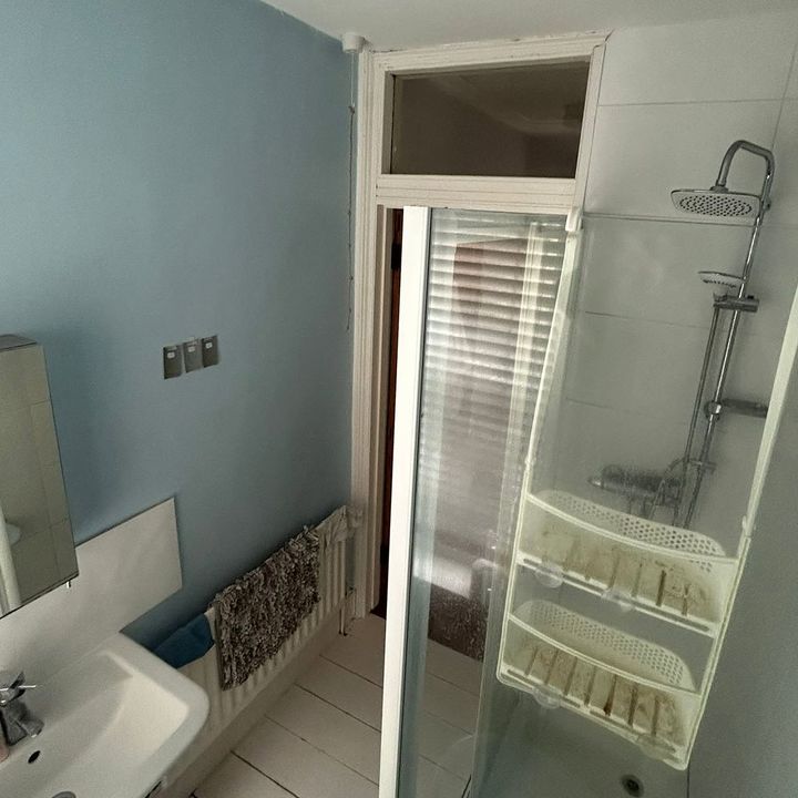 The shower room before: pale blue walls, a framed shower door and a fanlight over the doorway